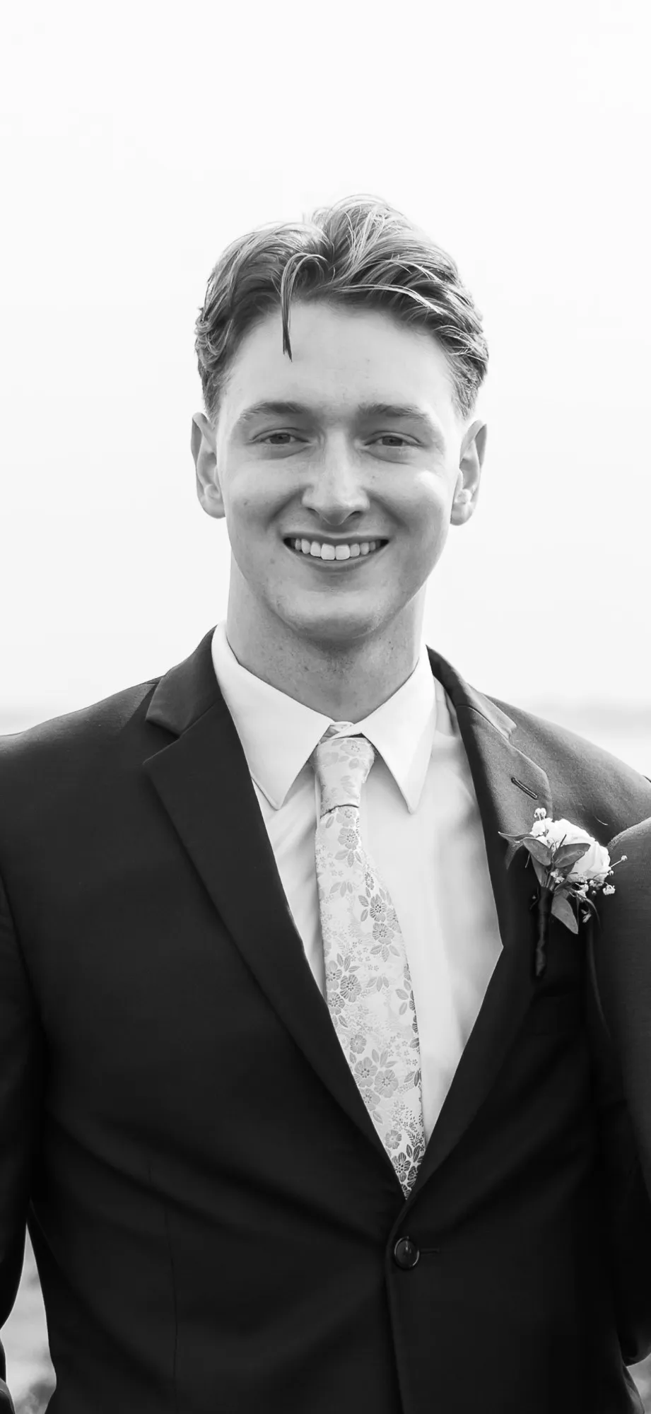Black-and-white photo of Sean Crowley smiling, wearing a dark suit and floral tie